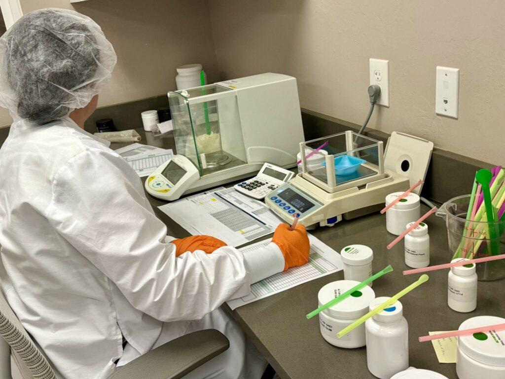 A formulator weighing raw ingredients against a batch record in the formulation lab
