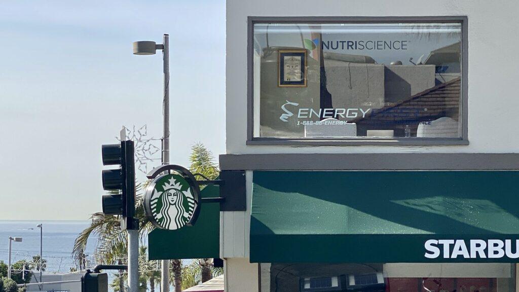 NutriScience and EnergyFirst signage in the office window above Manhattan Beach, with the Pacific Ocean beyond